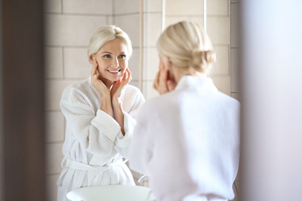 Beautiful senior older woman smiling looking at mirror. Skincare concept.